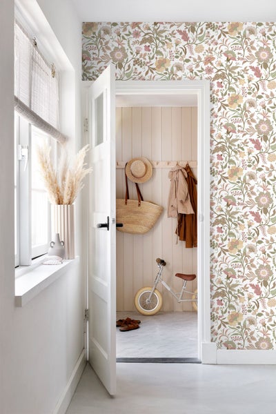 Helle Innenraumszene mit Vliestapete im Blumenmuster an der Wand, einer Tür und Blick in einen Raum mit Holzpaneelen.