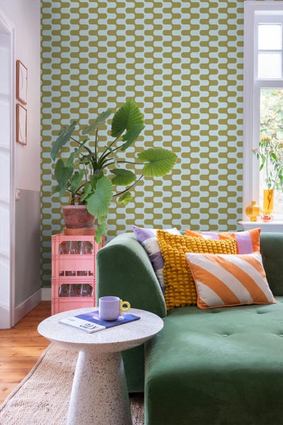 Wohnzimmer mit grüner Couch, gemusterter Tapete und Zimmerpflanze auf einem Beistelltisch