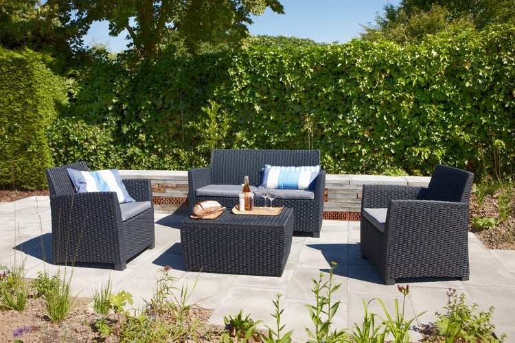 Gartenmöbel-Set aus Rattan mit Tisch, Sessel und Bank auf einer Terrasse.
