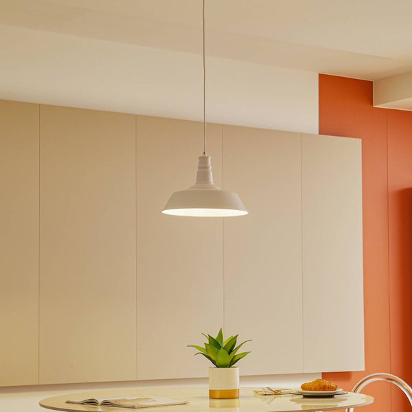 Industrielle Pendelleuchte mit weitem Schirm über einem Tisch mit Pflanze und Gebäck in einem hellen Raum.