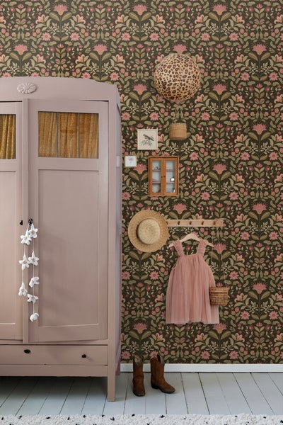 Dekorative Szene mit einer floral gemusterten Tapete, einem altrosa Schrank und Accessoires.