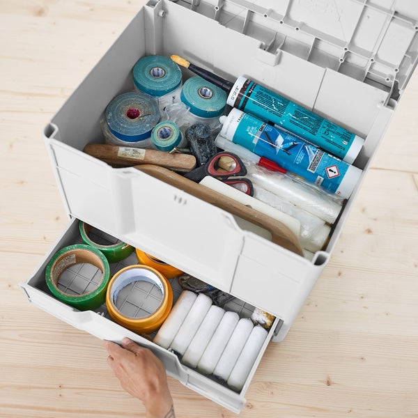Graue Werkzeugbox mit offenem Deckel und Schublade, gefüllt mit Abklebeband, Dichtstofftuben, Farbrollern und Werkzeug.