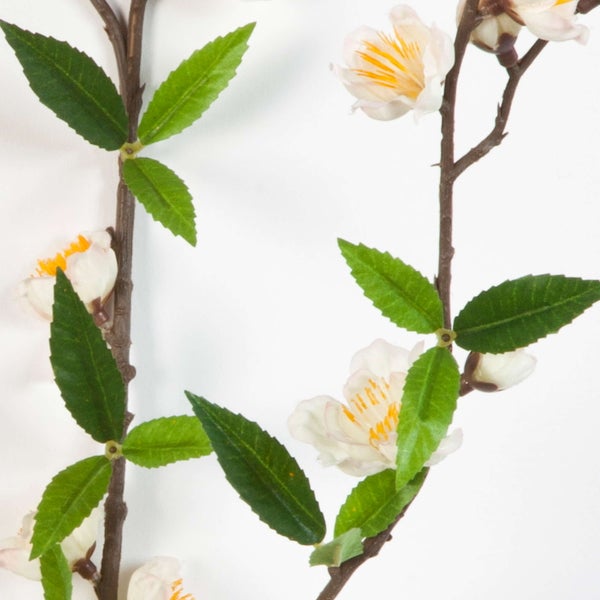 Künstlicher Blütenzweig mit weißen Blüten und grünen Blättern.