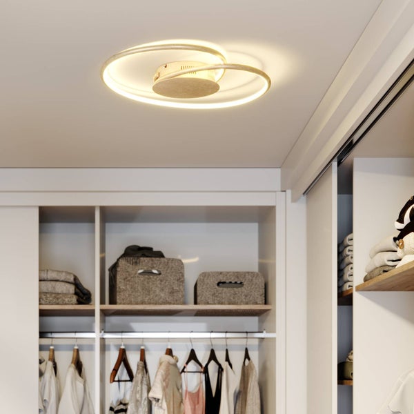 Moderne LED-Deckenleuchte mit zwei verschlungenen Ringen in einem hellen, organisierten Ankleidezimmer mit Regalen und Kleidung.