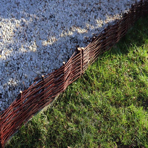 Gartenszene mit einem Zaun aus Haselnusszweigen, Kies und Rasenfläche
