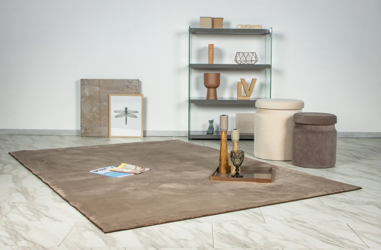 Wohnzimmer mit einem großen Teppich in gedeckten Tönen auf einem hellen Fliesenboden vor einem modernen Regal mit Dekoration und Sitzhockern.