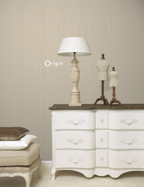 Szene mit Kommode, Lampe und Dekorationsfiguren vor einer strukturierten Tapete.