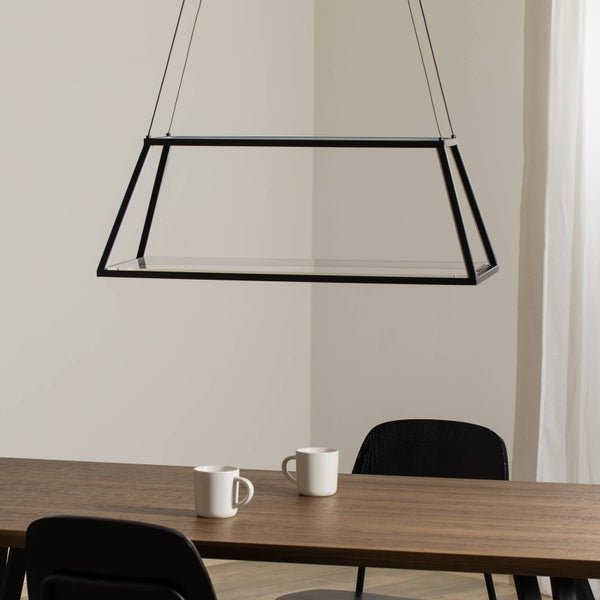 Moderne schwarze trapezförmige Pendelleuchte über einem hölzernen Esstisch mit weißen Tassen und schwarzen Stühlen in einem hellen Raum.