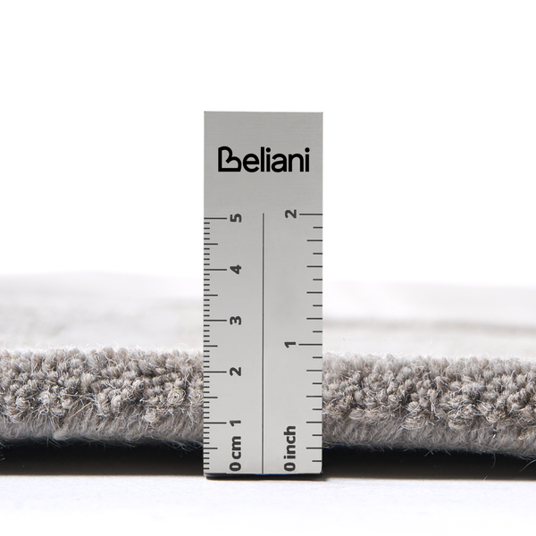 Ein Lineal mit dem Beliani Logo misst die Florhöhe eines Teppichs, die circa 1,5 Zentimeter beträgt.
