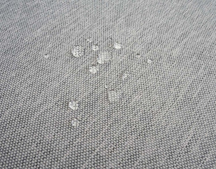 Wassertropfen perlen auf der Oberfläche eines wasserabweisenden Textilgewebes ab.