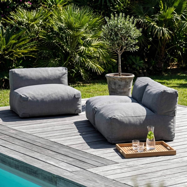 Gepolsterte graue Gartenloungemöbel auf einer Holzterrasse am Pool mit Pflanzen im Hintergrund.