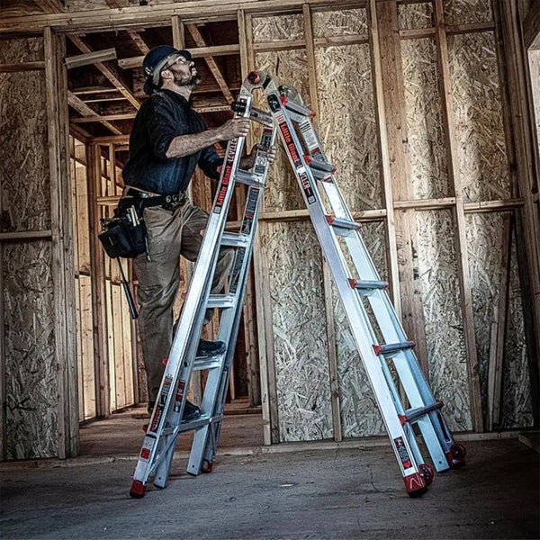 Handwerker mit Werkzeuggürtel auf einer Little Giant Mehrzweckleiter aus Aluminium in einem hellen Rohbau mit Holzrahmenwänden.