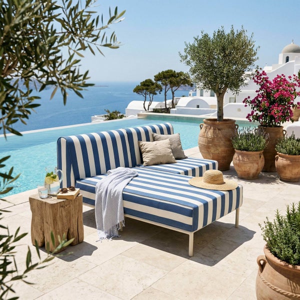 Loungesofa mit Streifenmuster auf Steinterrasse am Pool mit Meerblick, Beistelltisch aus Holz und Pflanzkübel aus Terrakotta im mediterranen Stil.