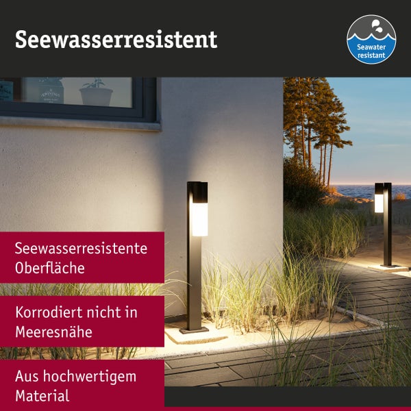 Zwei beleuchtete moderne Außenleuchten aus korrosionsbeständigem seewasserresistentem Material an einem gepflasterten Weg am Meer mit Dünengras.