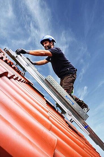 Ein Handwerker mit Schutzhelm auf einer Dachleiter auf einem Ziegeldach