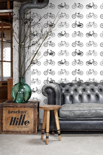 Ein Wohnzimmer mit einem Sofa, einem Hocker, einer Holzkiste, einer Glasvase und einer Tapete mit Fahrradmuster.