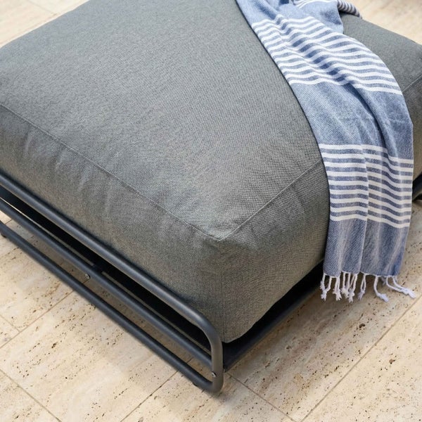 Grauer Outdoor-Hocker mit Metallgestell und Polsterkissen, dekoriert mit einem gestreiften Tuch.