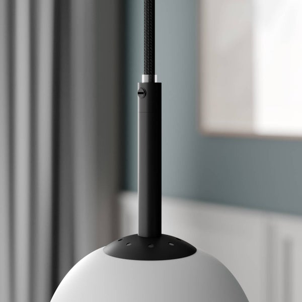 Detailaufnahme einer Pendelleuchte mit schwarzem Textilkabel, schwarzer Metallaufhängung und weißem Kugelschirm aus Glas.
