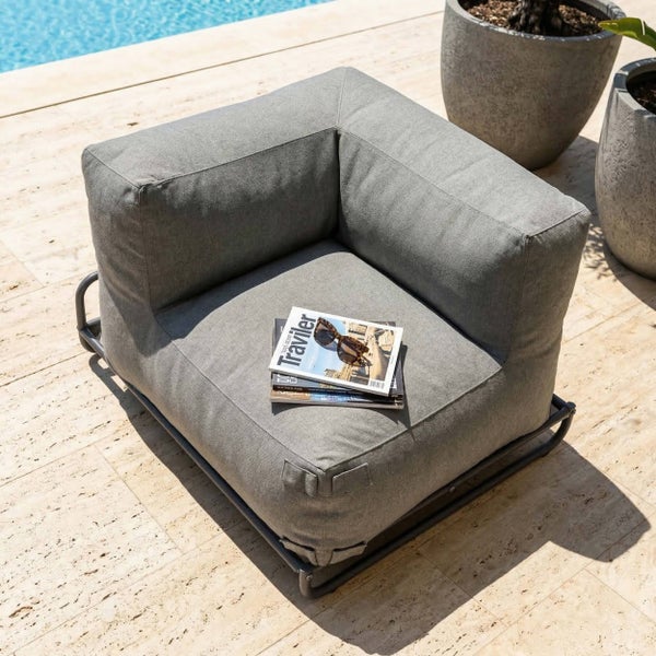Grauer Garten-Lounge-Ecksessel mit Metallgestell auf einer hellen Steinterrasse neben einem Pool.