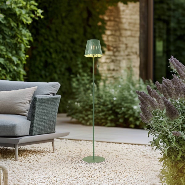 Moderne Stehleuchte für den Außenbereich mit perforiertem Schirm auf einer Terrasse mit Kieselsteinen, Gartenmöbeln und Pflanzen.