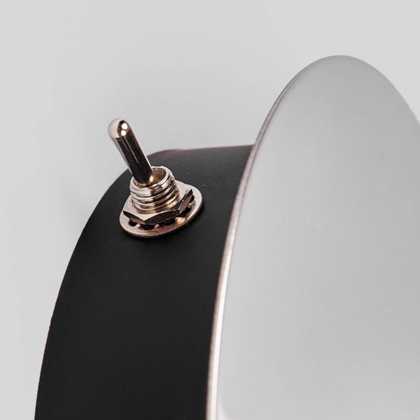 Nahaufnahme eines metallischen Kippschalters an einer schwarzen runden Leuchte.