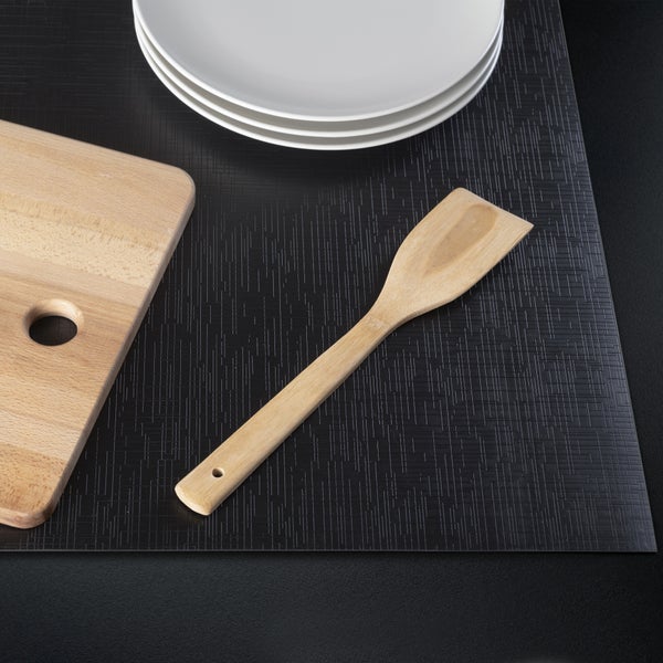 Schwarze strukturierte Küchenmatte mit einem Pfannenwender aus Holz, einem Schneidebrett aus Holz und gestapelten Tellern.