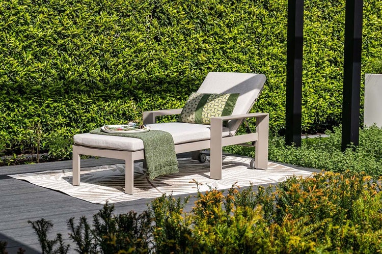 Gartenmöbel-Set mit verstellbarer Sonnenliege und Hocker inklusive Polsterauflagen auf einer Terrasse vor einer Hecke.