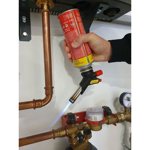 Hand hält einen Rothenberger Industrial Gasbrenner mit Butankartusche beim Erhitzen eines Kupferrohrs.