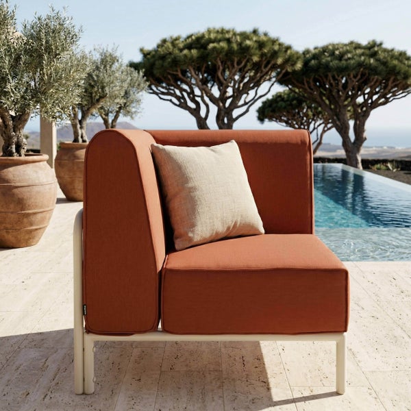 Modernes Gartensofa Eckmodul mit rostfarbenem Polster und hellem Kissen auf einer hellen Terrasse am Pool.
