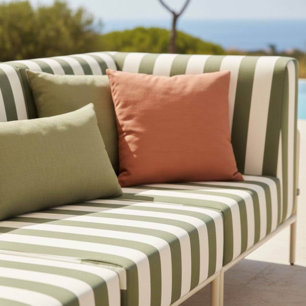 Gestreiftes Outdoor-Sofa mit grünen und terrakottafarbenen Dekokissen auf einer Terrasse.