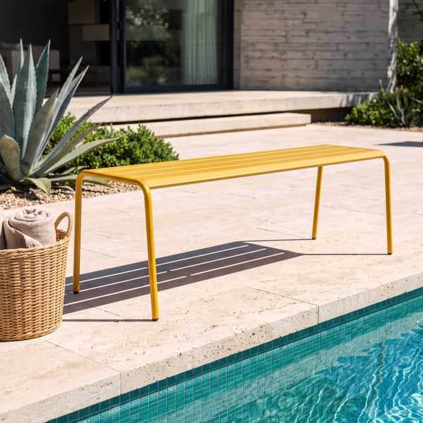 Gelbe Gartenbank aus Metall in modernem Design auf einer hellen Steinterrasse am Pool mit geflochtenem Korb.