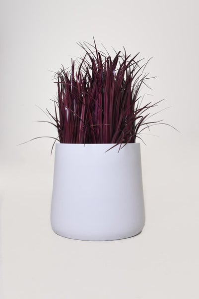 Künstliches Dekogras in Lila in einem weißen Blumentopf.