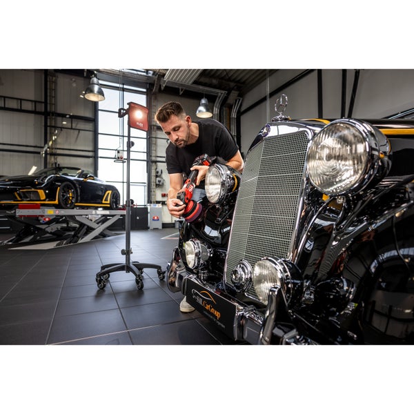 Ein Handwerker poliert mit einer Akku Poliermaschine die Karosserie eines Oldtimers in einer professionellen Werkstatt mit Arbeitsleuchte.
