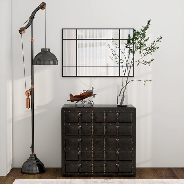 Industrielle Inneneinrichtung mit einer Kommode in Kofferoptik, einer schwarzen Stehleuchte mit Flaschenzug und einem Wandspiegel mit Sprossen.