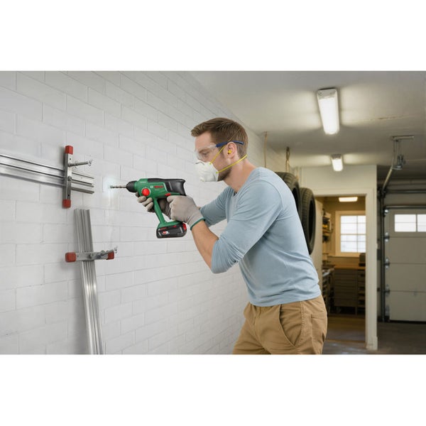Ein Handwerker bohrt mit einem Bosch Akku Bohrhammer in eine weiße Ziegelwand in einer Werkstatt.