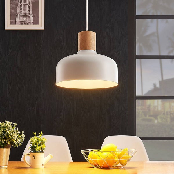 Moderne Pendelleuchte mit weißem Metallschirm und Holzaufsatz hängend über einem Esstisch mit Obstschale und Pflanzen.