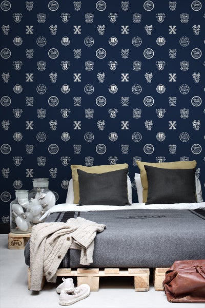 Schlafzimmer mit Bett und dunkelblauer Tapete mit College-Motiven