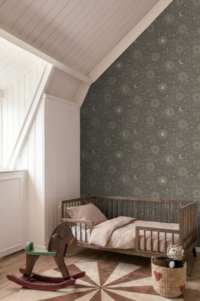 Kinderzimmer mit Tapete mit Sonnen-, Mond- und Sternenmuster, einem Kinderbett aus Holz und einem Schaukelpferd.