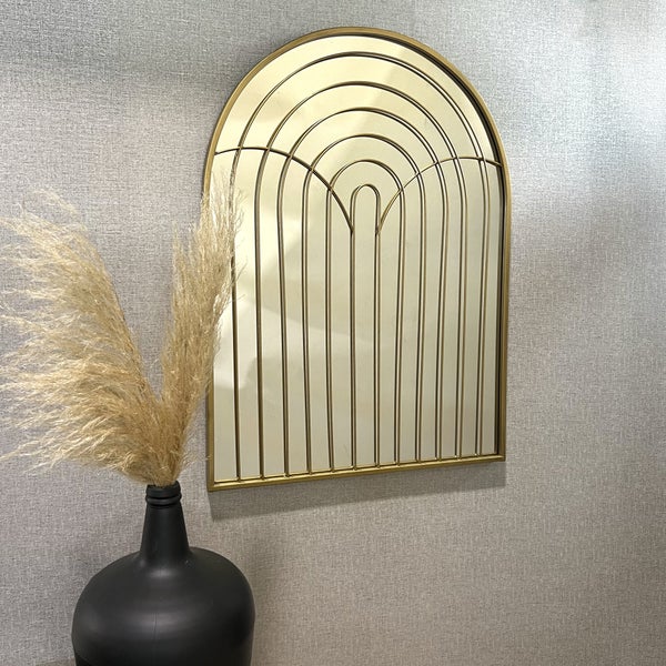 Bogenförmiger Wandspiegel mit goldfarbenem Metallrahmen und dekorativem Muster aus konzentrischen Bögen und vertikalen Linien.