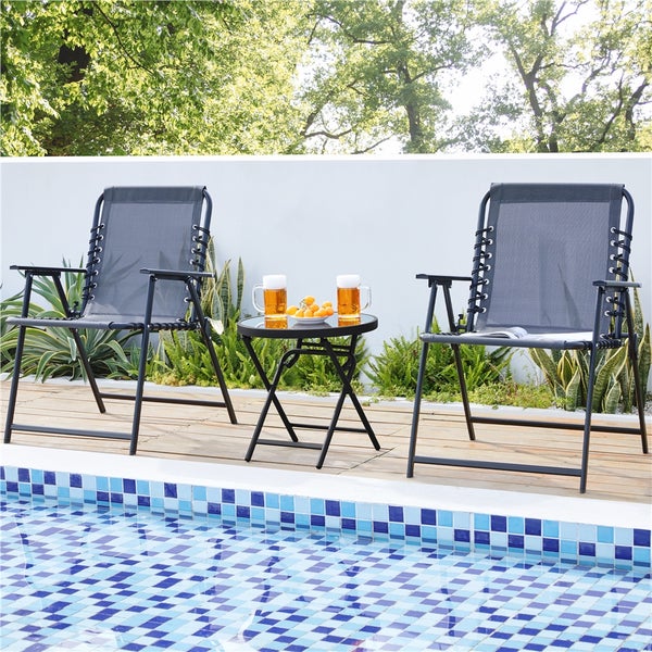 Zwei graue Gartenklappstühle und ein kleiner schwarzer Beistelltisch auf einer Holzterrasse neben einem blau gefliesten Swimmingpool.