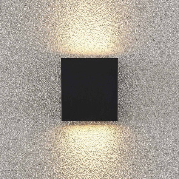 Quadratische Wandleuchte in Schwarz mit Lichtaustritt nach oben und unten an einer strukturierten Wand.