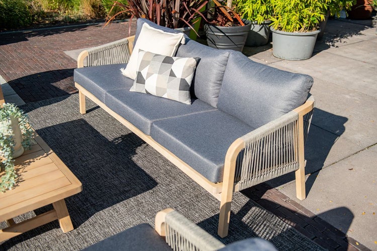 Modernes Gartensofa aus Holz mit grauen Polstern und Seilbespannung auf einer Terrasse neben einem passenden Holztisch.