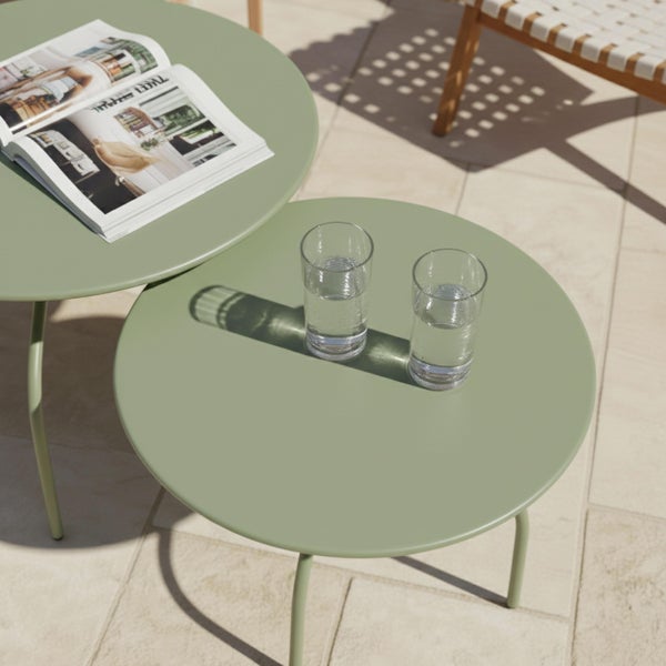 Zwei runde grüne Beistelltische aus Metall im Set auf einer Terrasse mit zwei Wassergläsern und einer Zeitschrift.