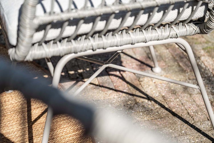 Detailaufnahme eines Gartenstuhls mit grauem Kunststoffgeflecht und einem hellgrauen Metallgestell auf einer Terrasse.
