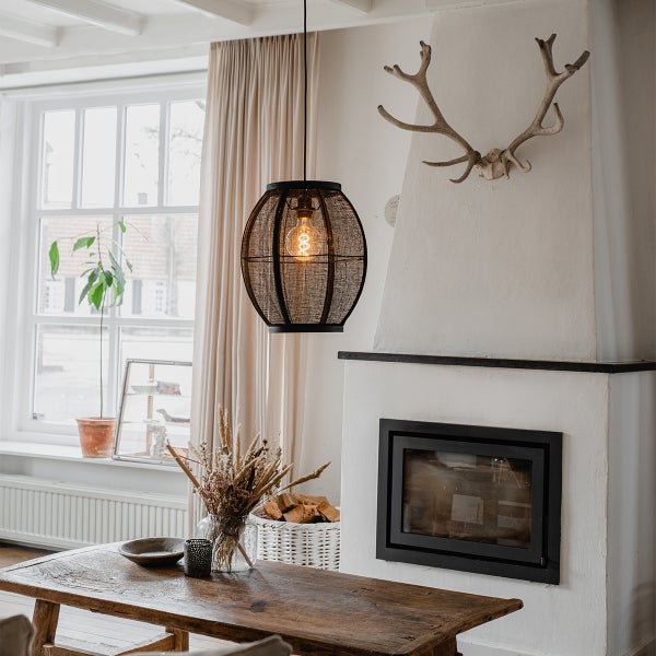 Moderne Pendelleuchte mit Netzschirm über einem rustikalen Holztisch in einem Wohnraum mit Kamin und Hirschgeweih an der Wand.