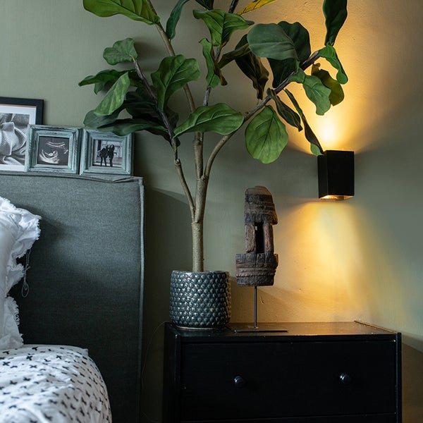 Schlafzimmer mit Bett, Kommode, Zimmerpflanze und Wandleuchte