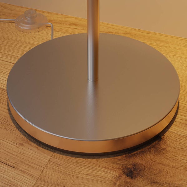 Runder Metallsockel einer Stehleuchte mit kupferfarbenem Rand und Fußschalter auf Holzboden.