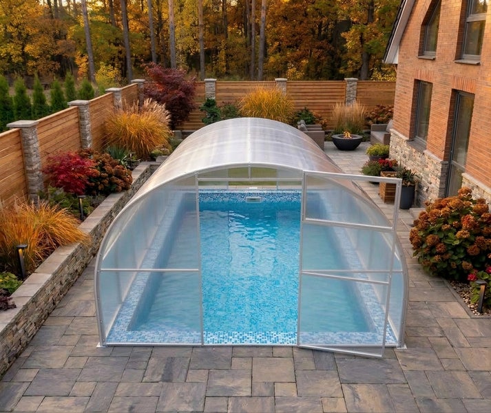 Rechteckiger Pool mit teilweiser Überdachung durch ein gewölbtes Schiebedach aus Polycarbonat auf einer Terrasse im Garten neben einem Wohnhaus