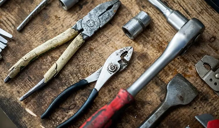 Verschiedene Handwerkzeuge wie Zangen, eine Ratsche und Aufsätze auf einer Holzwerkbank ausgelegt.
