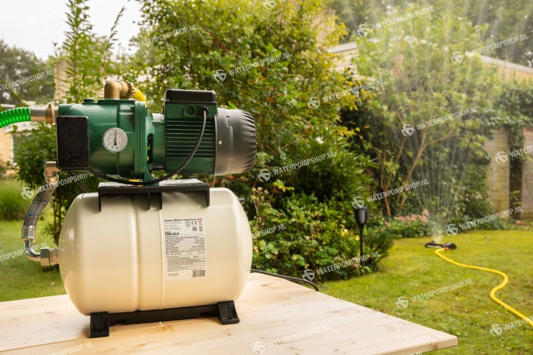 Hauswasserwerk auf einem Holztisch mit Rasensprenger im Hintergrund